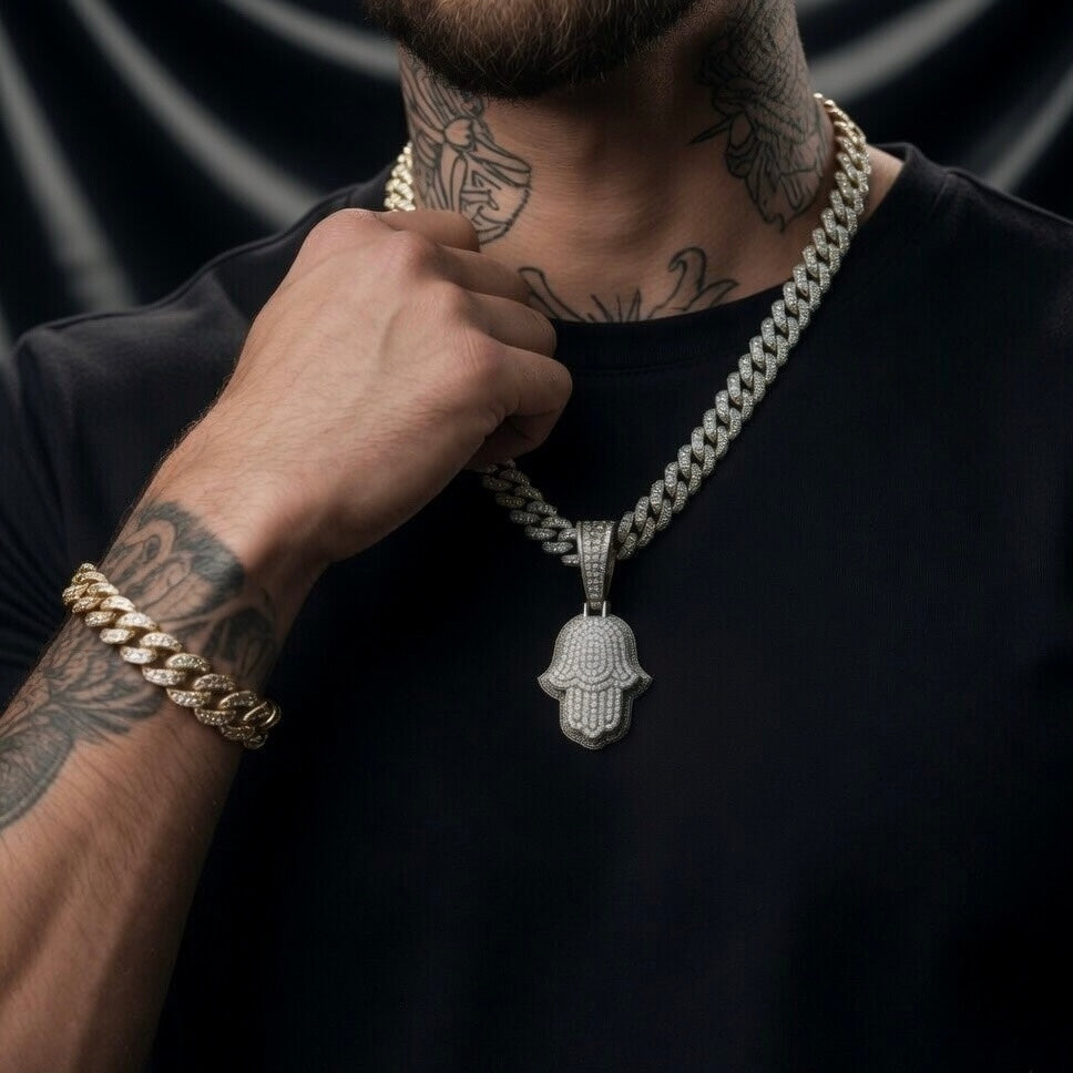 Man wearing a gold chain necklace with a silver moissanite Hamsa hand pendant on a black background