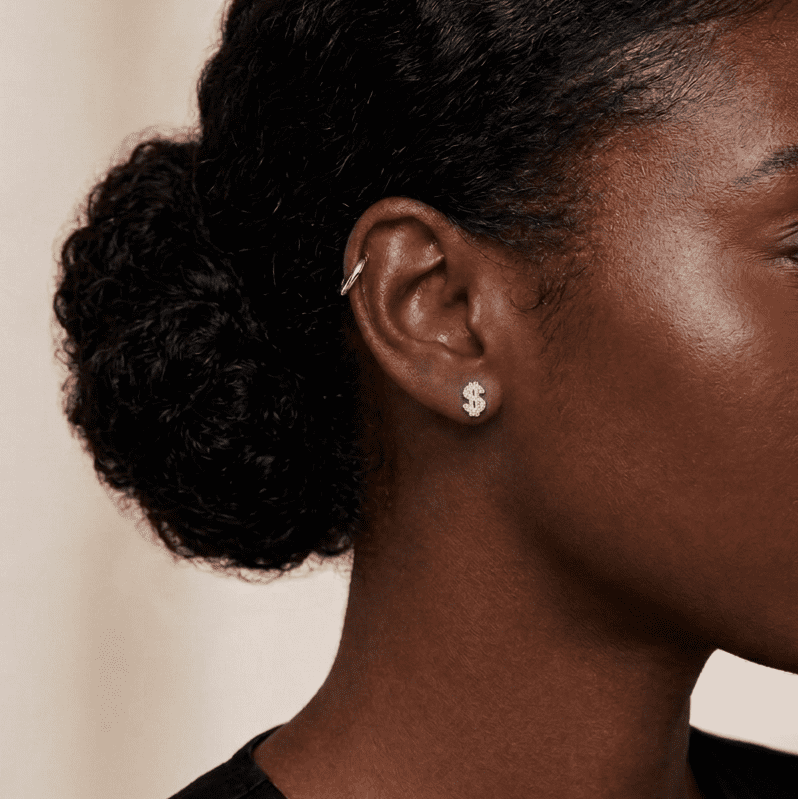 Close-up of a person wearing dollar shape moissanite earrings with a neutral background