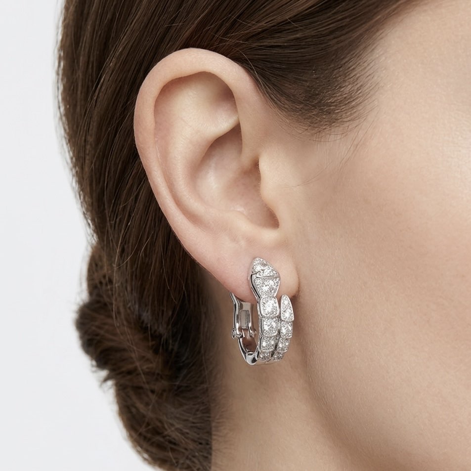 Close-up of a person wearing a silver hoop earring with clear gemstones on a neutral background