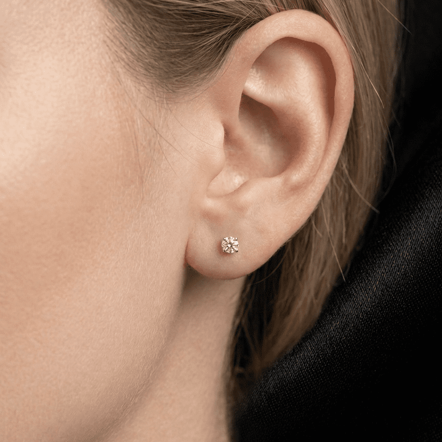Close-up of an ear wearing a small diamond earring with a black background