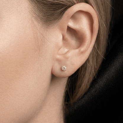 Close-up of an ear wearing a small diamond earring with a black background