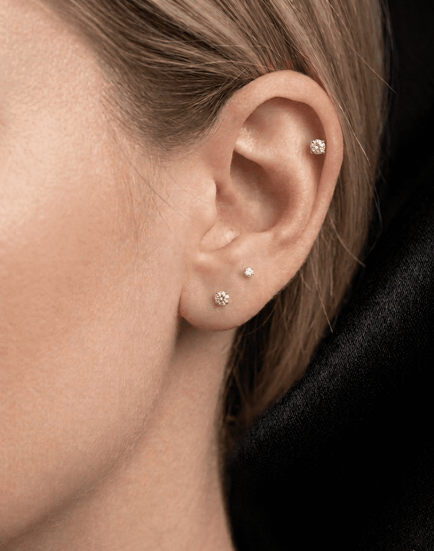 Close-up of an ear with mossanite stud earrings against a neutral background