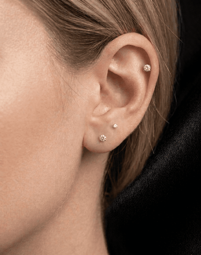 Close-up of an ear with mossanite stud earrings against a neutral background