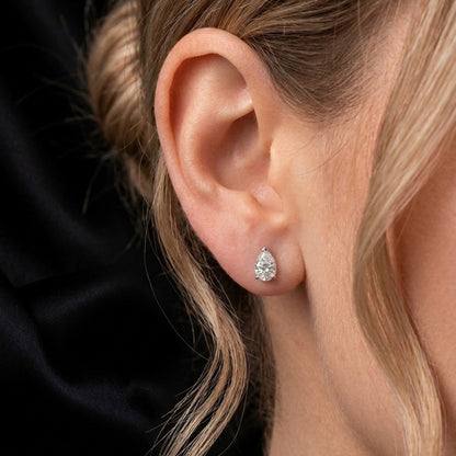 Close-up of a person wearing a teardrop-shaped diamond earring.