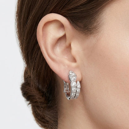 Close-up of a person wearing a silver hoop earring with clear gemstones on a neutral background
