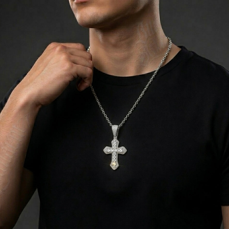 Man wearing a black shirt with a silver moissanite cross pendant necklace against a dark background