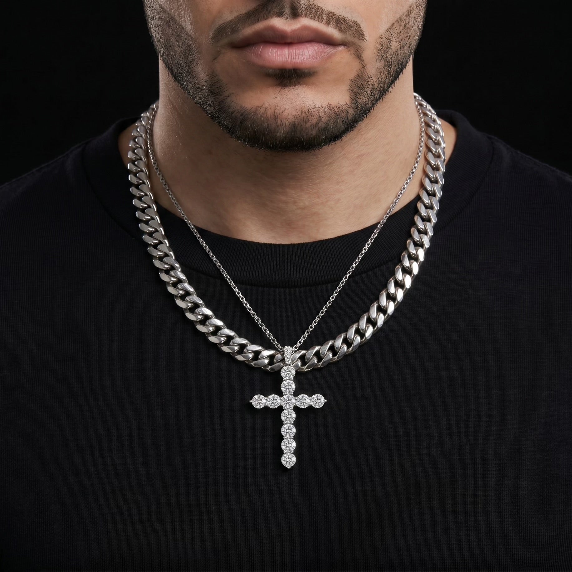 Man wearing a black shirt with two silver chain necklaces and a cross pendant.