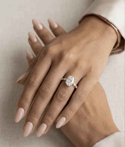 Hand wearing a oval diamond ring on a neutral background